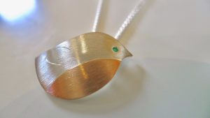 Closeup of a baby Robin created in rose gold and silver, and set with an emerald