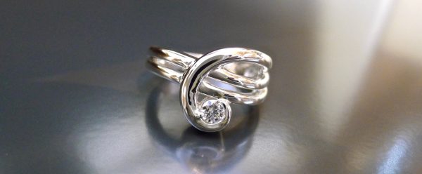 Precious metal formed into a ribbon and forged into a ring that swirls up to hold a perfect diamond