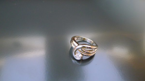 A continous ribbon of precious metal swirls up and around your finger to hold a 1/5 carat stunning diamond A continous ribbon of precious metal swirls up and around your finger to hold a 1/5 carat stunning diamond